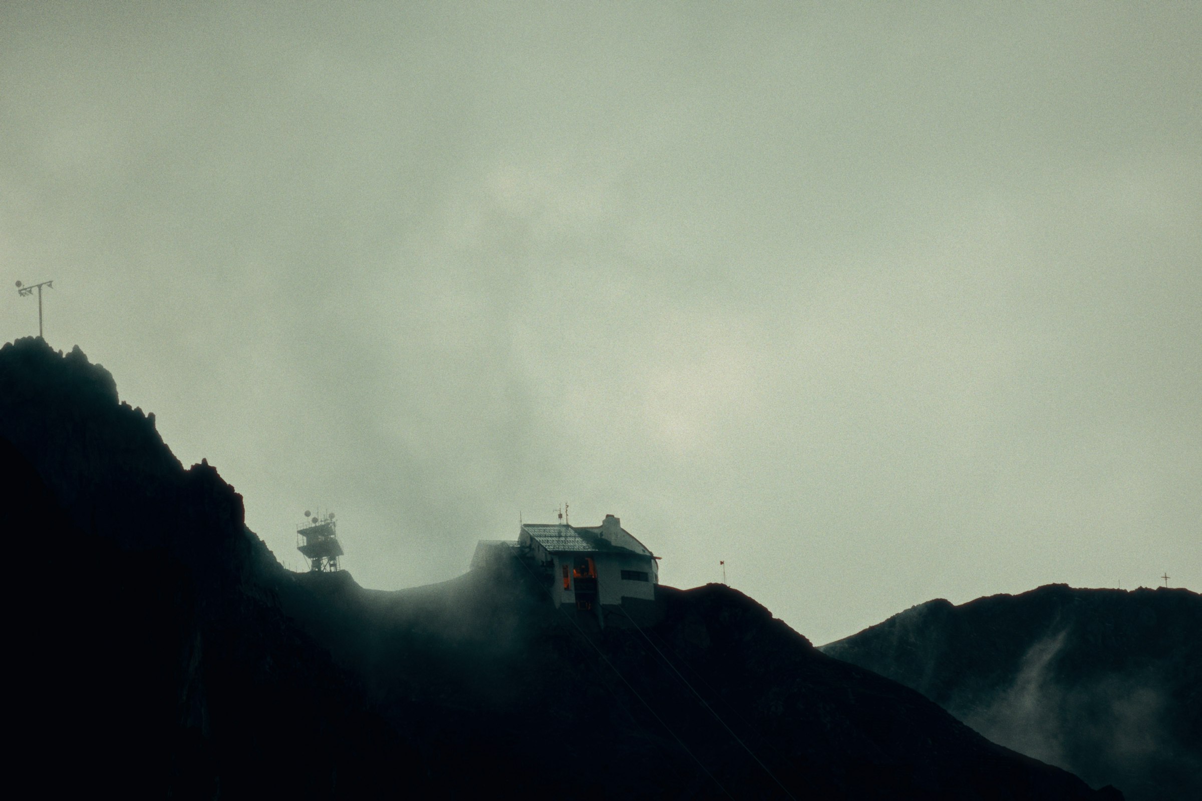 A small building on a dark, foggy mountain slope by Florian Schindler