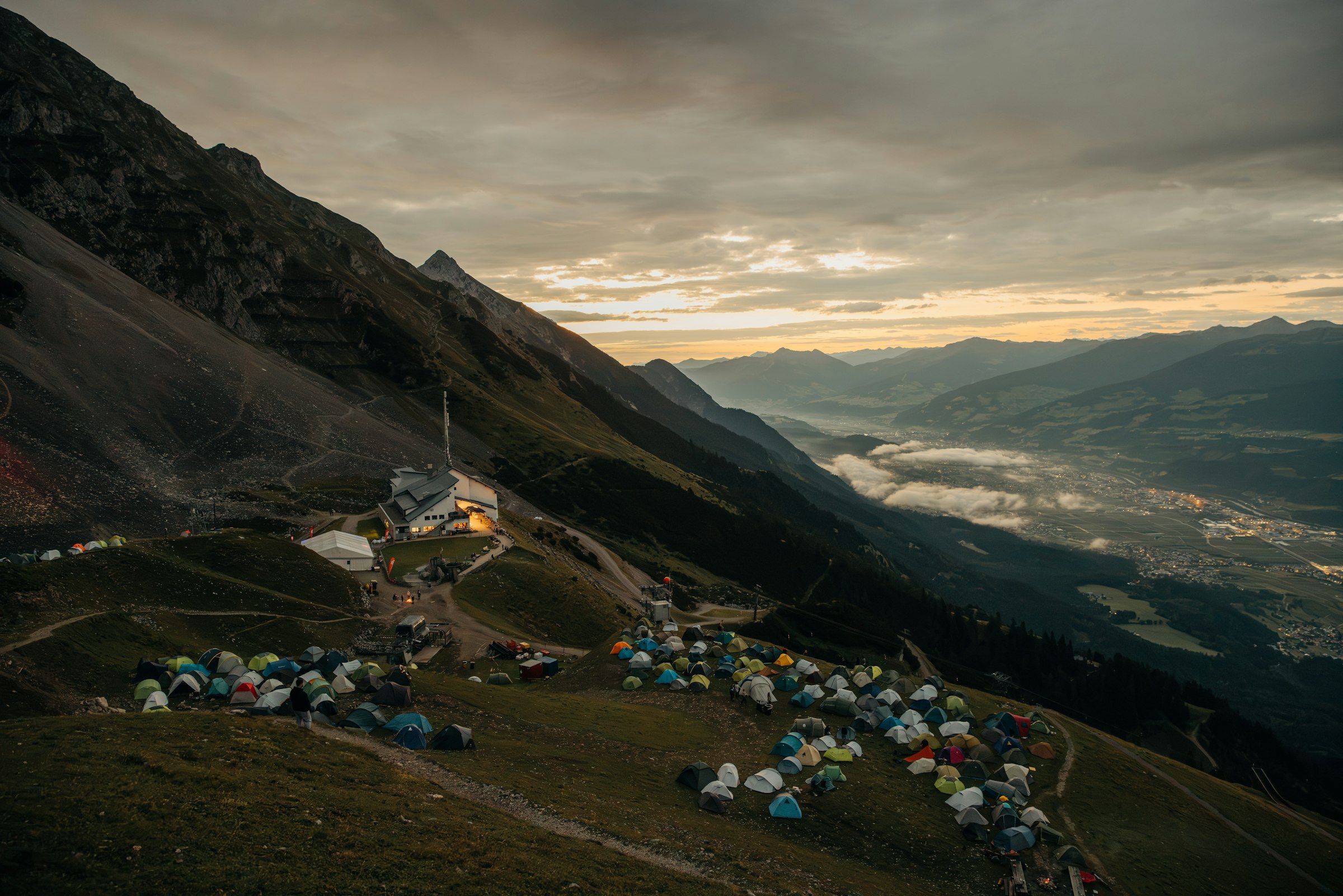 A mountain campsite with many tents overlooking a valley at dusk by Florian Schindler