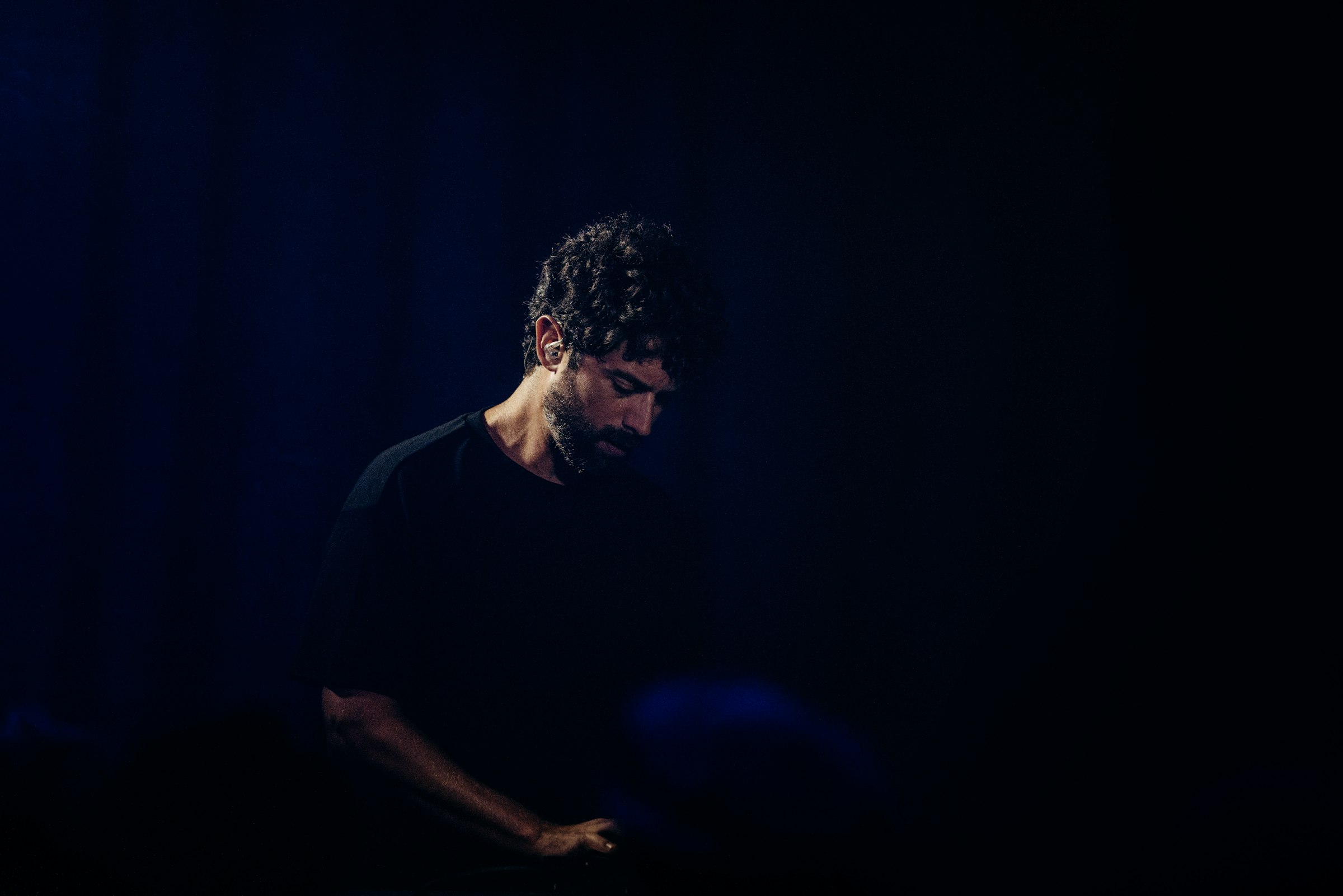 A man with curly hair looking down in darkness at a night event by Florian Schindler