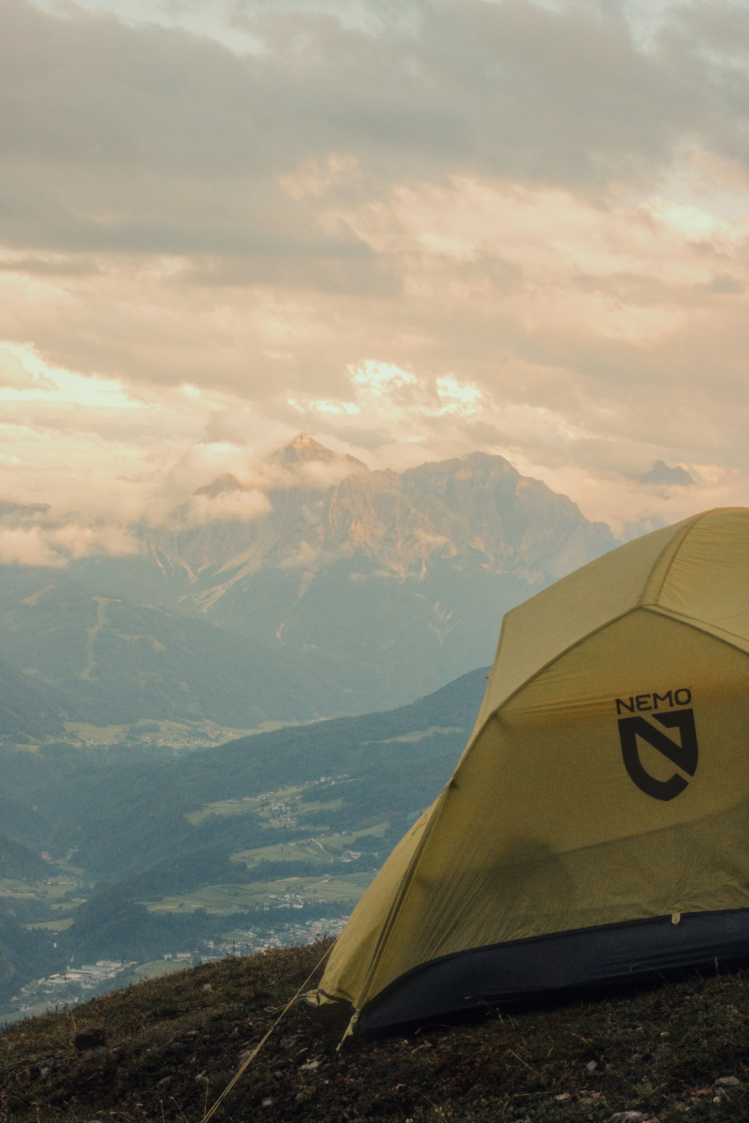 A yellow camping tent on a mountain with cloudy peaks by Florian Schindler