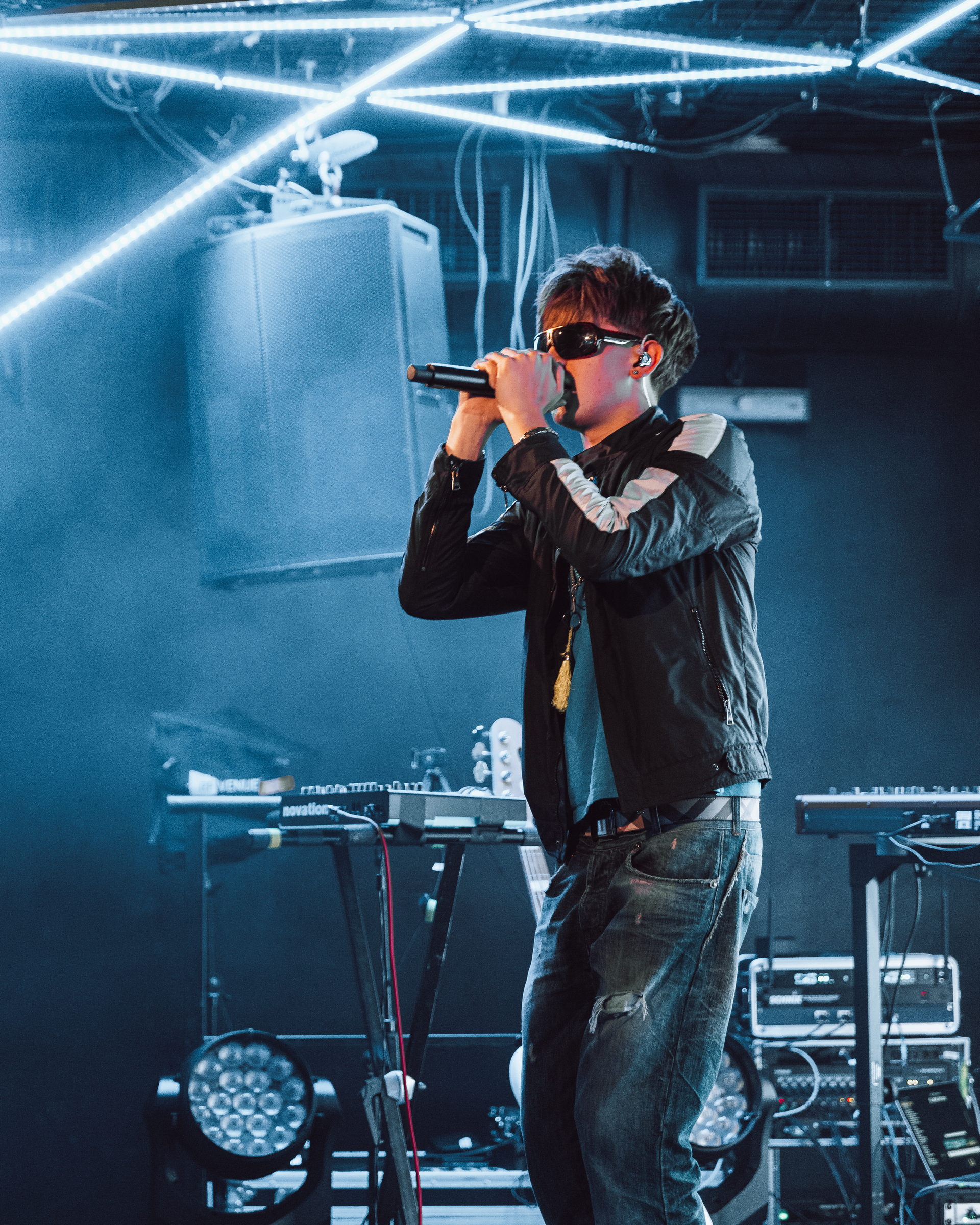 A singer in sunglasses holding the microphone close on a club stage under white LED strips by Florian Schindler