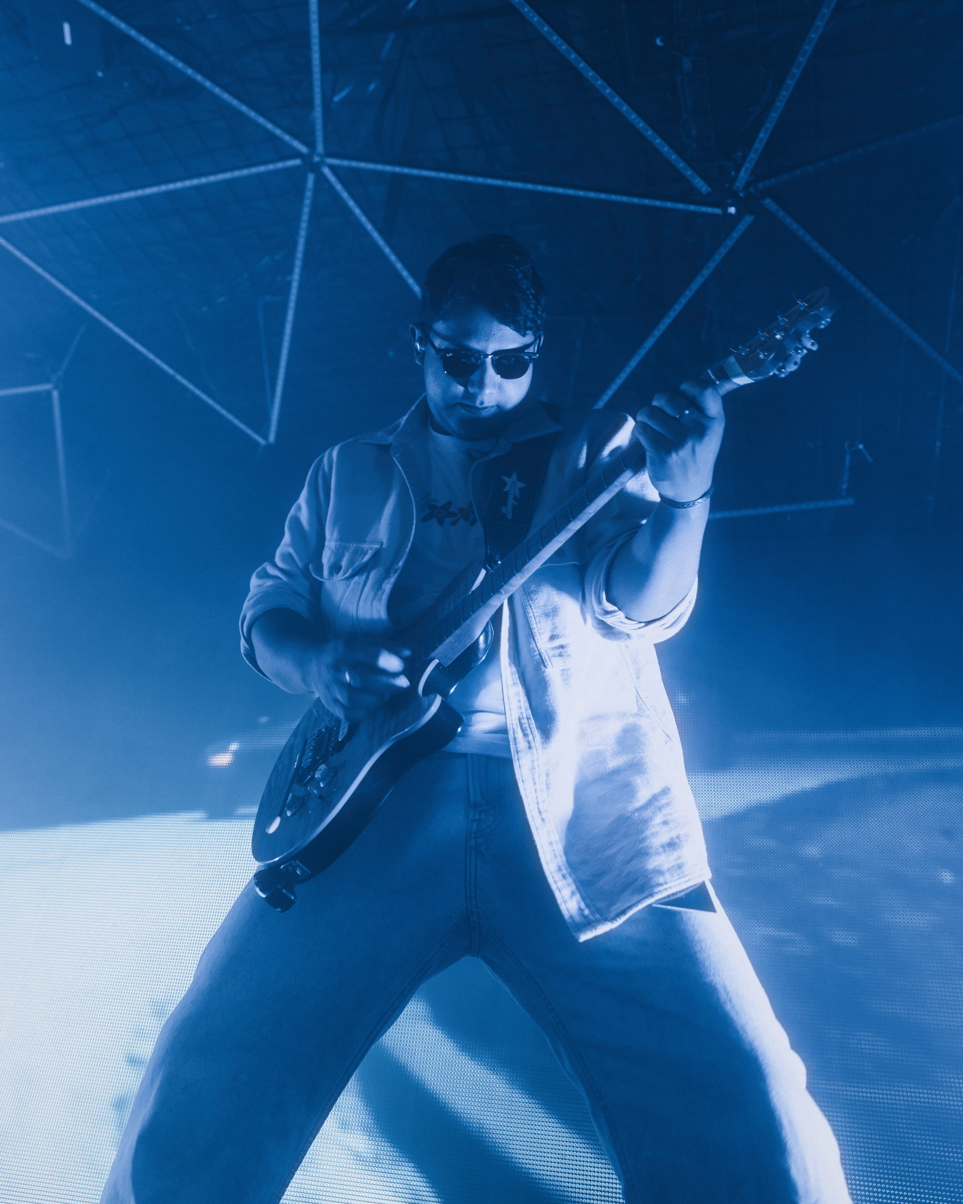A guitarist in sunglasses playing in deep blue stage light, seen from a low angle by Florian Schindler