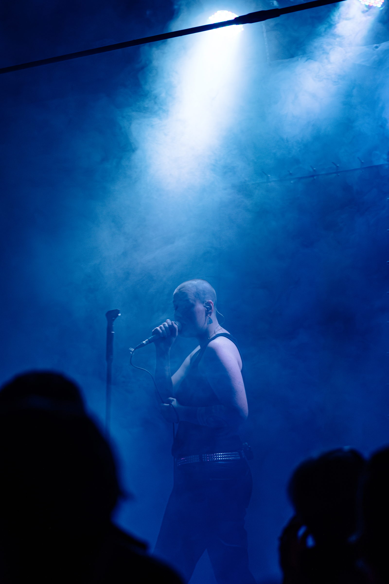 A singer at the microphone under a single blue spotlight cutting through smoke by Florian Schindler
