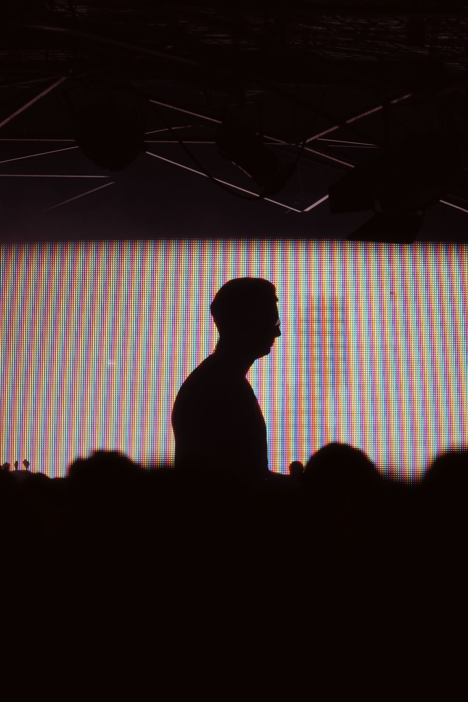 A silhouette in profile against a glowing LED wall above the heads of a crowd by Florian Schindler