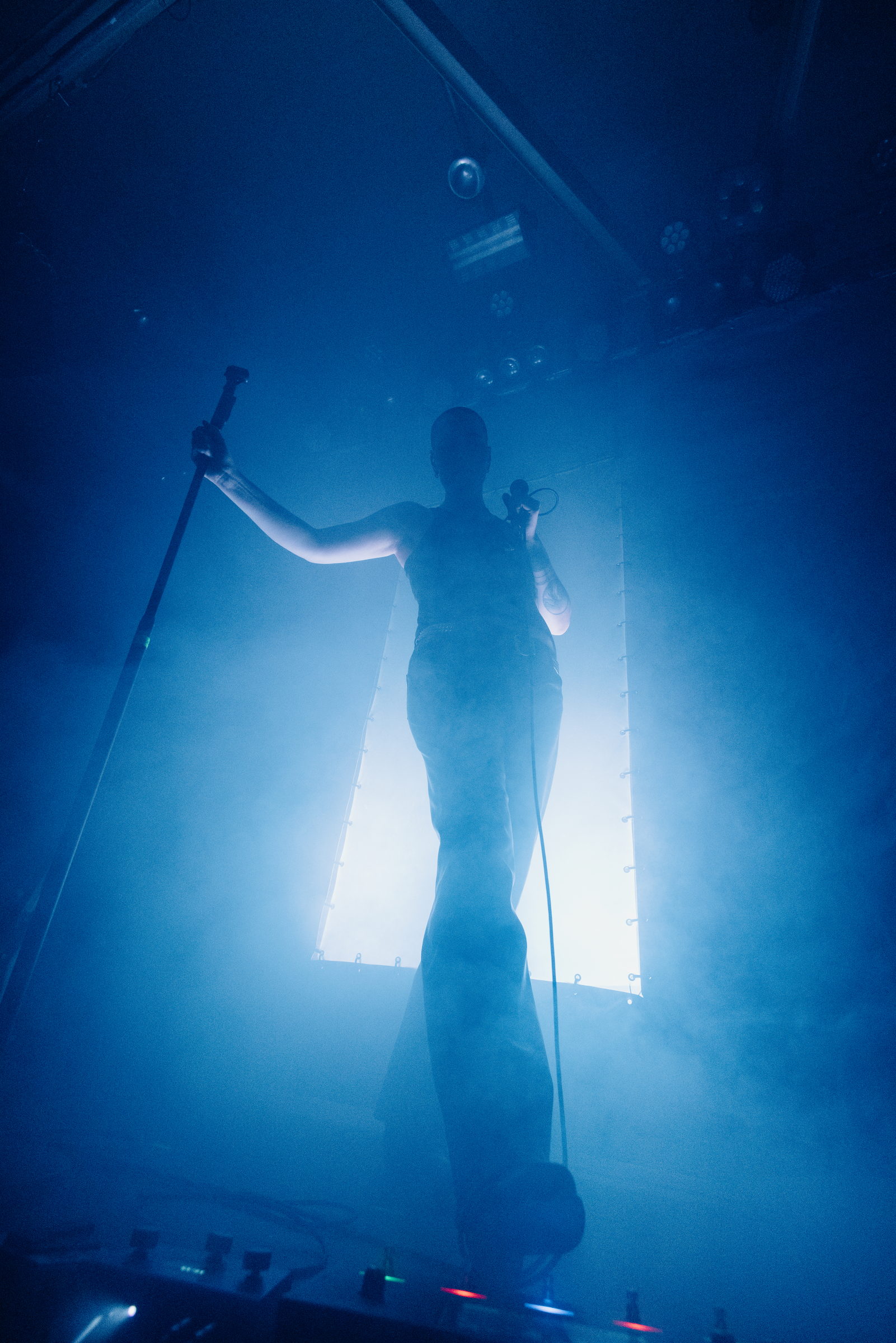 A singer silhouetted against a bright panel in blue fog, holding a microphone stand by Florian Schindler